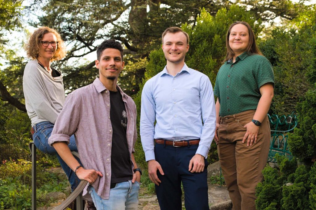 Four members of the Nelson Lab standing beside a stair railing in a wooded garden.