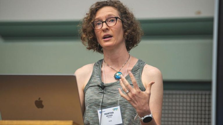 Martha Nelson gesturing as she speaks to an audience, wearing a conference lanyard. Credit: Michelle Bixby / Penn State, Creative Commons.