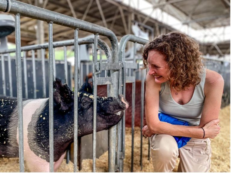 Martha Nelson crouched at the rails of a pen at a county fair, laughing face to face with a black-and-white show pig. Credit: J. Cohen / Science.